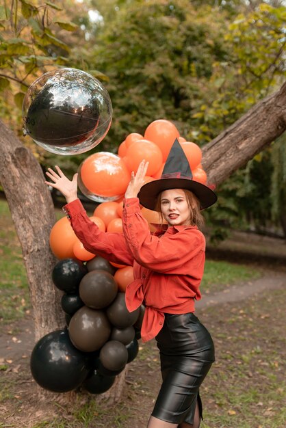 Beautiful girl in orange shirt, black skirt and witch hat. Will throw up a balloon. Smile. Halloween