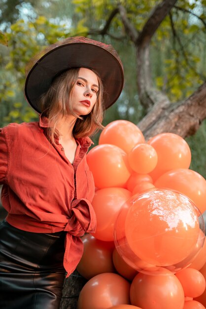 A beautiful girl in orange shirt, black skirt and a witch's hat. She looks at the camera. Halloween