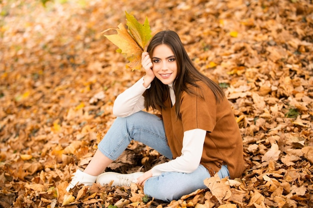 Beautiful girl outdoors in autumn fall young woman collects yellow fall leaves in autumn beauty woma