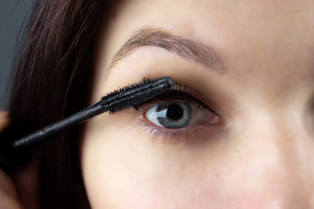 Beautiful girl paints eyes with mascara close-up