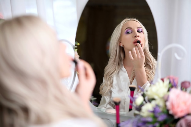 A beautiful girl paints her lips in front of a mirror.