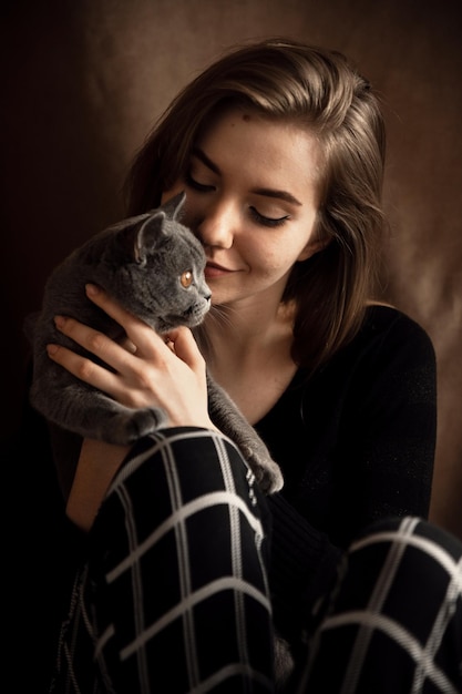 A beautiful girl in pajamas sits on a chair and affectionately\
hugs a kitten of a scottish breed cute and smiling girl at home\
hugging a domestic cat domestic gray british cat