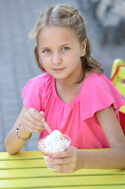 Beautiful girl in a pink t-shirt sits at a yellow table and eats ice cream