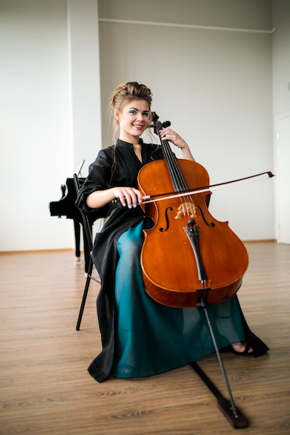 A beautiful girl plays the cello in the classroom the cello plays and smiles at the camera