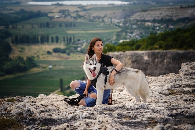 Красивая девушка играет с собакой, серый и белый хаски, в горах на закате. Индийская девушка и ее волк
