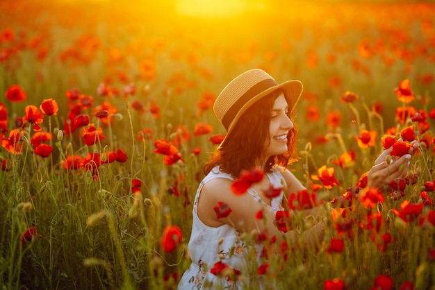 Beautiful girl in the poppy field at sunset in a white dress and hat