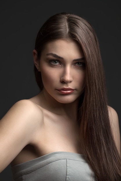 The beautiful girl poses in studio on a gray background. fashion portrait. make-up. long hair.