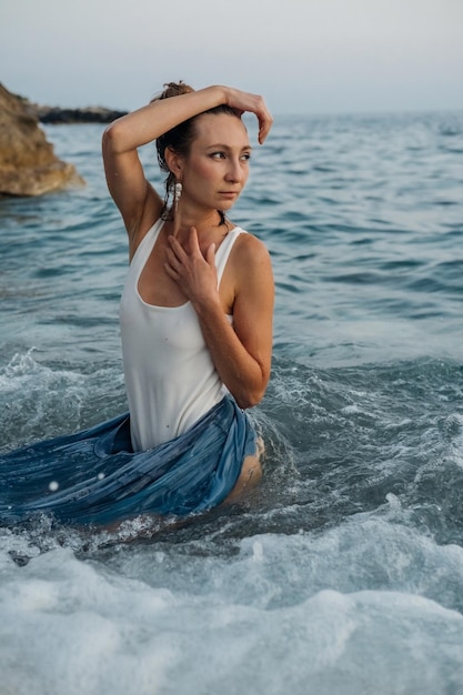 Foto bella ragazza che posa sulle onde del mare in una sessione fotografica di moda serale in natura