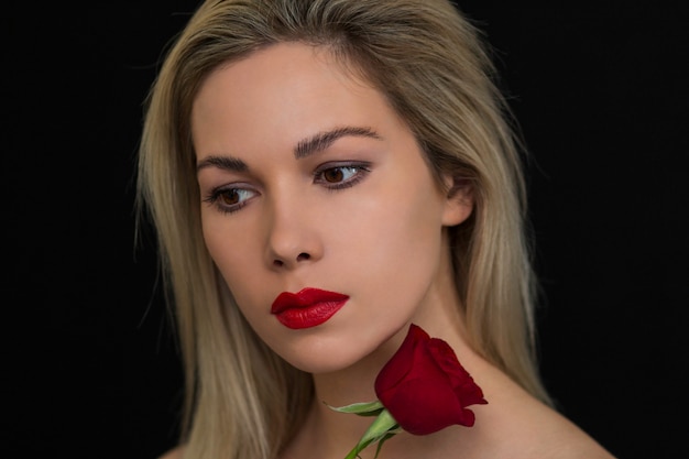 Bella ragazza che posa con una rosa rossa su un'oscurità