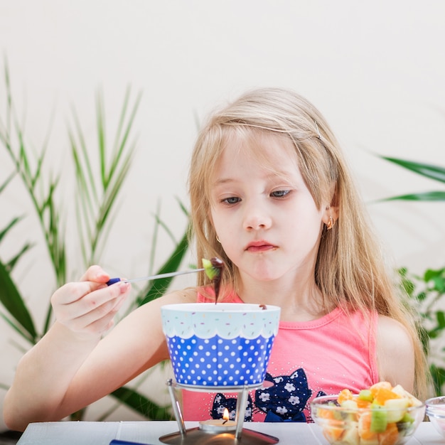 美しい少女は、キウイフルーツとチョコレートフォンデュを準備します。