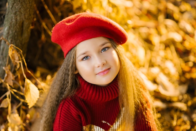 Beautiful girl in a red beret is sitting near a tree in autumn