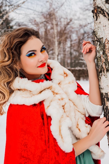 Beautiful girl in a red cape in the winter forest