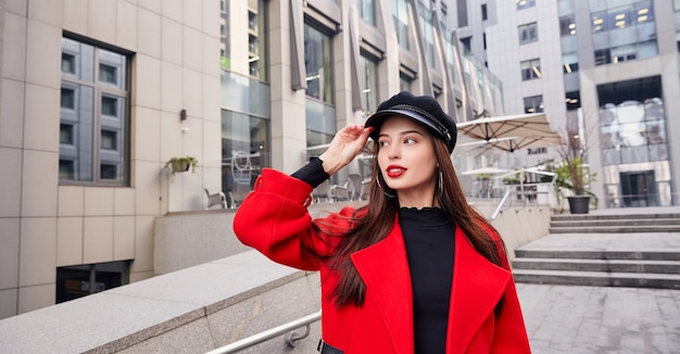 Beautiful girl in a red coat and a black hat in the street