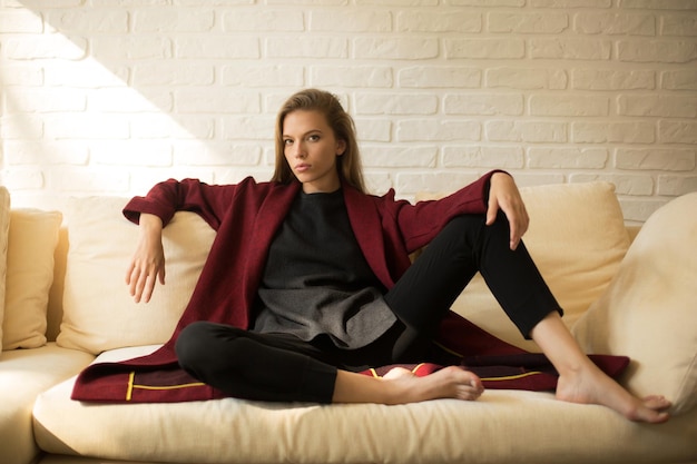 Photo beautiful girl in a red coat having a rest on the sofa