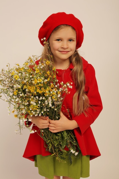 a beautiful girl in a red coat and a red beret holds wildflowers in her hands