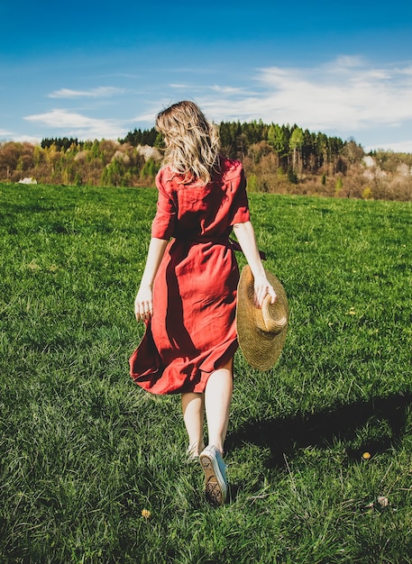 Beautiful girl in red dress and hat have a carefree time on meadow in mountains by a forest  Spring season
