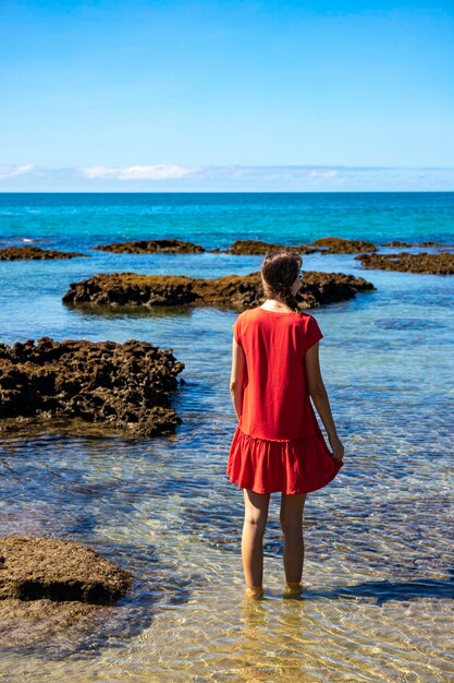 beautiful girl in red dress stands in coral reef water in daintree national park, australia