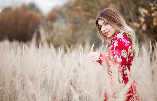 Beautiful girl in a red dress walks among the high grass in the field