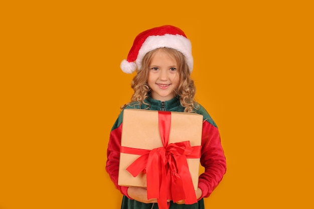 a beautiful girl in a red and green Santa Claus hat dress holds a gift box in her hands