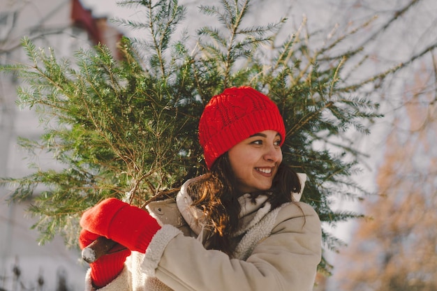 A beautiful girl in a red hat carries a christmas tree
