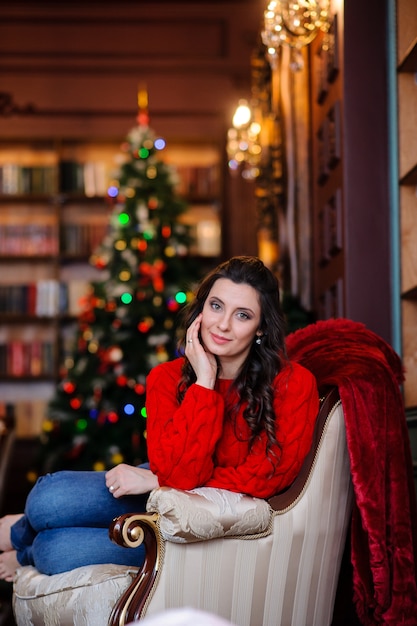 Beautiful girl in a red sweater near the Christmas tree.