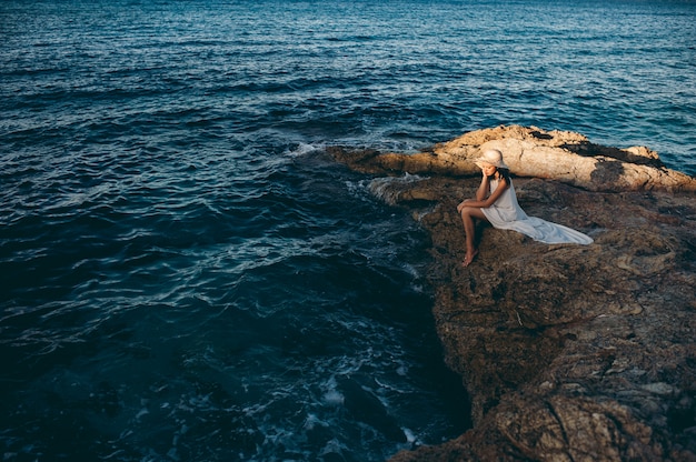 Photo beautiful girl relaxes on the rock on the coast mole