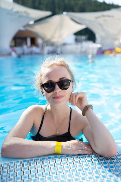 Beautiful girl relaxes in the swimming pool in sunny day