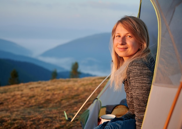 Beautiful girl resting in tent on the blurred background of mountain hills