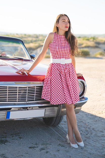 Photo beautiful girl in a retro dress at sunrise happy posing on the background of the mountain landscape in cappadocia near a red retro car