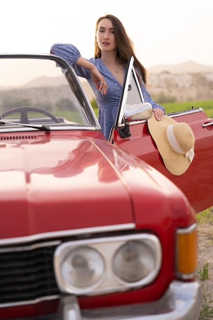 Foto bella ragazza in stile retrò in posa vicino a un'auto cabriolet rossa d'epoca