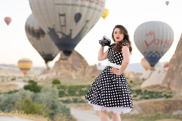 Beautiful girl in retro style posing with old film camera on background of hot air balloons in Cappadocia