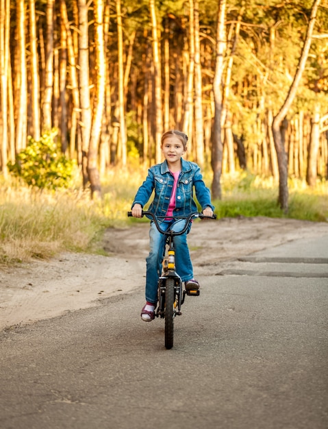 森の道路で彼女の自転車に乗って美しい少女