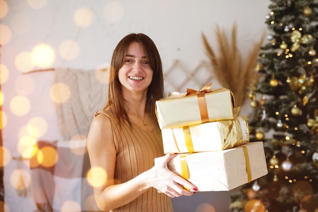 Bella ragazza in camera con regalo in involucro d'oro vicino all'albero di natale