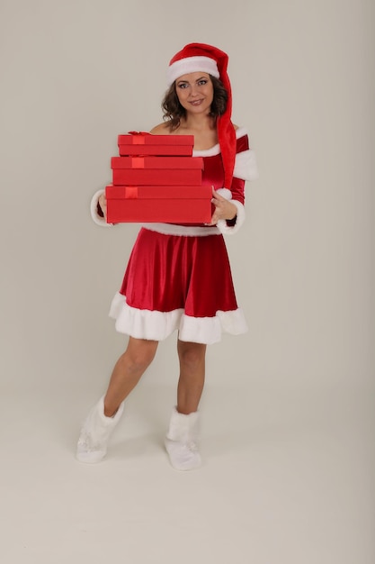красивая девушка в шапке Деда Мороза и костюме Снегурочки держит в руках подарочные коробки