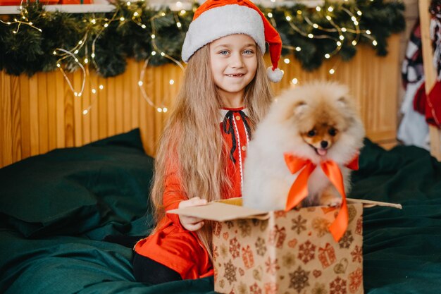 Красивая девочка в шапке Санты получила щенка в подарок на Новый год, рождественское волшебство и чудо, мечты сбываются.
