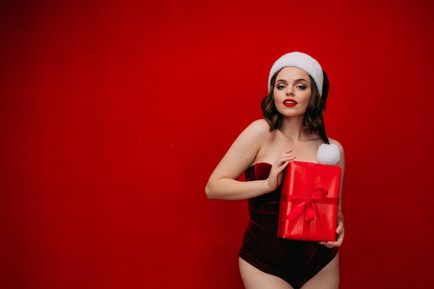 A beautiful girl in a Santa hat holds a New Years gift in her hands on a red background