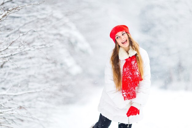 Beautiful girl show grimaces in white and red winter clothes in park covered with snow