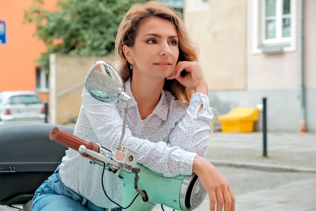 Foto una bella ragazza siede su un motorino da città, la ragazza punta lo sguardo verso l'annuncio