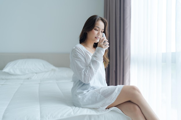 A beautiful girl sits drinking water smiling happily in the white bedroom
