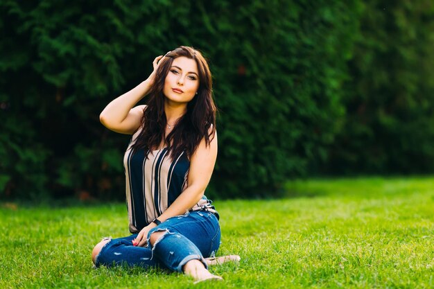 A beautiful girl sits on the grass in the park look at camera