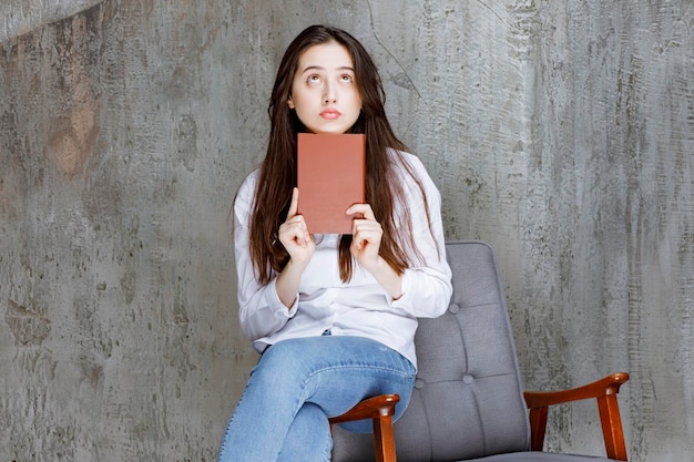 Beautiful girl sitting on armchair and holding book. High quality photo