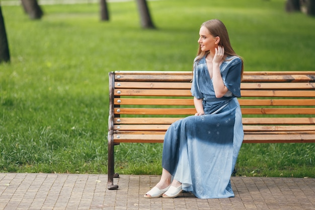 ベンチに座っている美しい少女、明るいドレスを着たブルネット、公園で晴れた日、公園で夏休み。日当たりの良い春