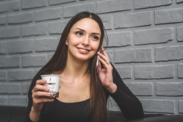 Beautiful girl sitting on a leather sofa in the salon drinking coffee and talking on the phone