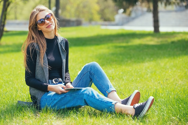 写真 夏の間にタブレットで草の上に座っている美しい少女。