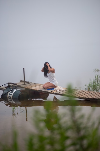 Beautiful girl sitting on the pier by the river