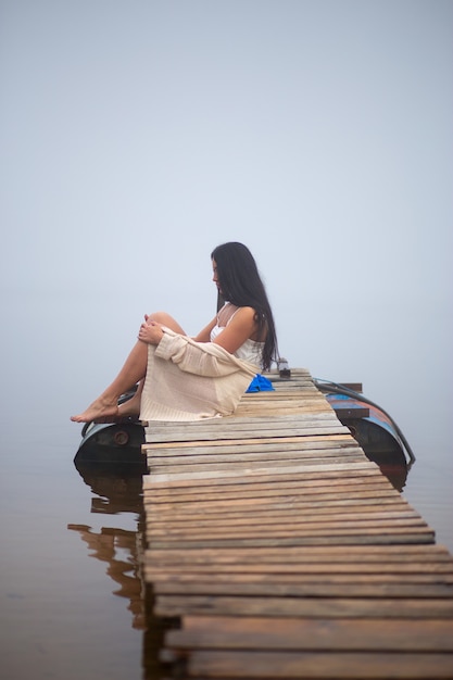 Beautiful girl sitting on the pier by the river