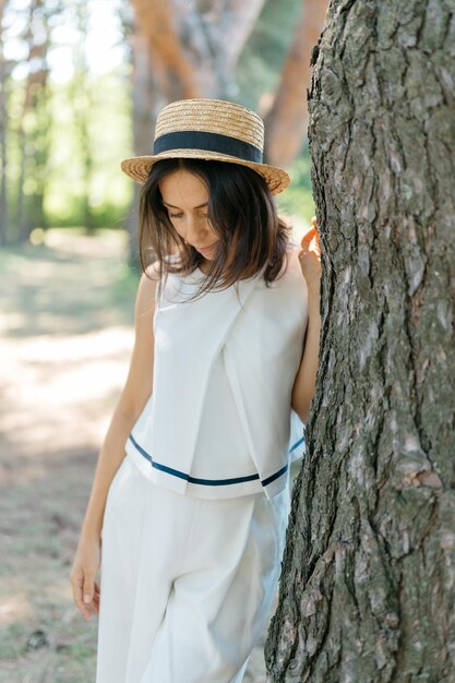 Beautiful girl in small straw hat and in white suit in the big public park soft focus and blur