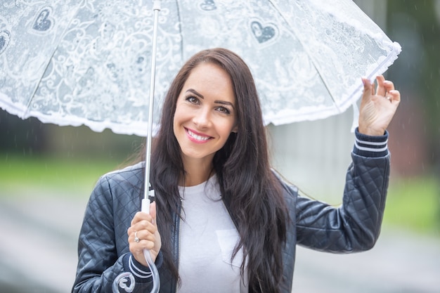 아름 다운 소녀는 비에서 그녀를 보호 하기 위해 우산을 들고 카메라에 미소.