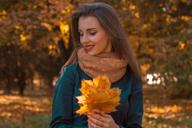 Beautiful girl smiling and holding a maple leaf in the hands closeup