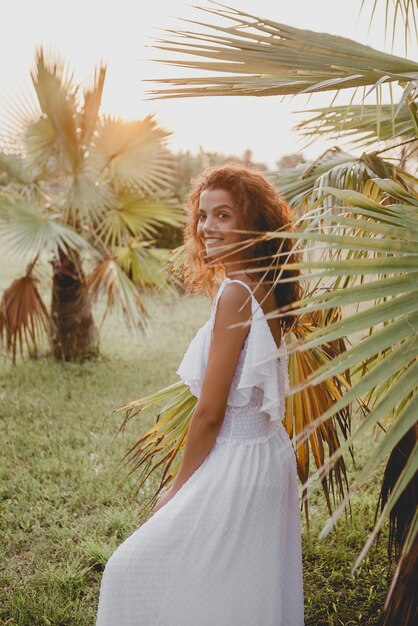 Beautiful girl smiling near palm trees in a white dress